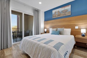 A hotel room with a large bed, a wooden headboard, a balcony with chairs, and a painting on the wall.