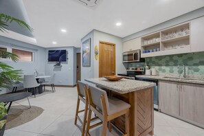 A modern kitchen with a central island, a dining area with a table and chairs, and a kitchen counter with a microwave and cabinets.