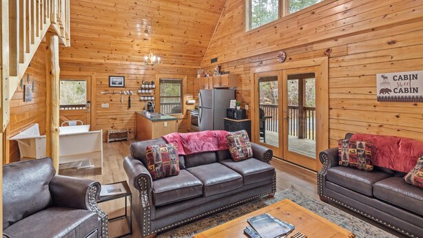 A cabin interior with wooden walls, a sofa, a coffee table, and a kitchen area. - SMOKY MTN STAYS OFF LAKE w/POOL & HOT TUB (Sevierville)