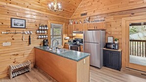 A wooden cabin kitchen with a central island, stainless steel appliances, and a hanging light fixture. - SMOKY MTN STAYS OFF LAKE w/POOL & HOT TUB (Sevierville)