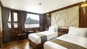 Quarto de hotel com duas camas, piso de madeira, vista para um corpo d'água e janela com cortinas.