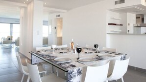 A modern dining area with a glass table, white chairs, and a central light fixture.