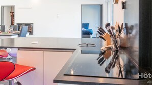 A modern kitchen with a central island, a dining area with chairs, and a visible bed in the background. - La Vedrenne: Smart Barn near Limoges (Bonnac-la-Côte)