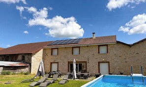 A stone building with a tiled roof, solar panels, a swimming pool, and outdoor seating.