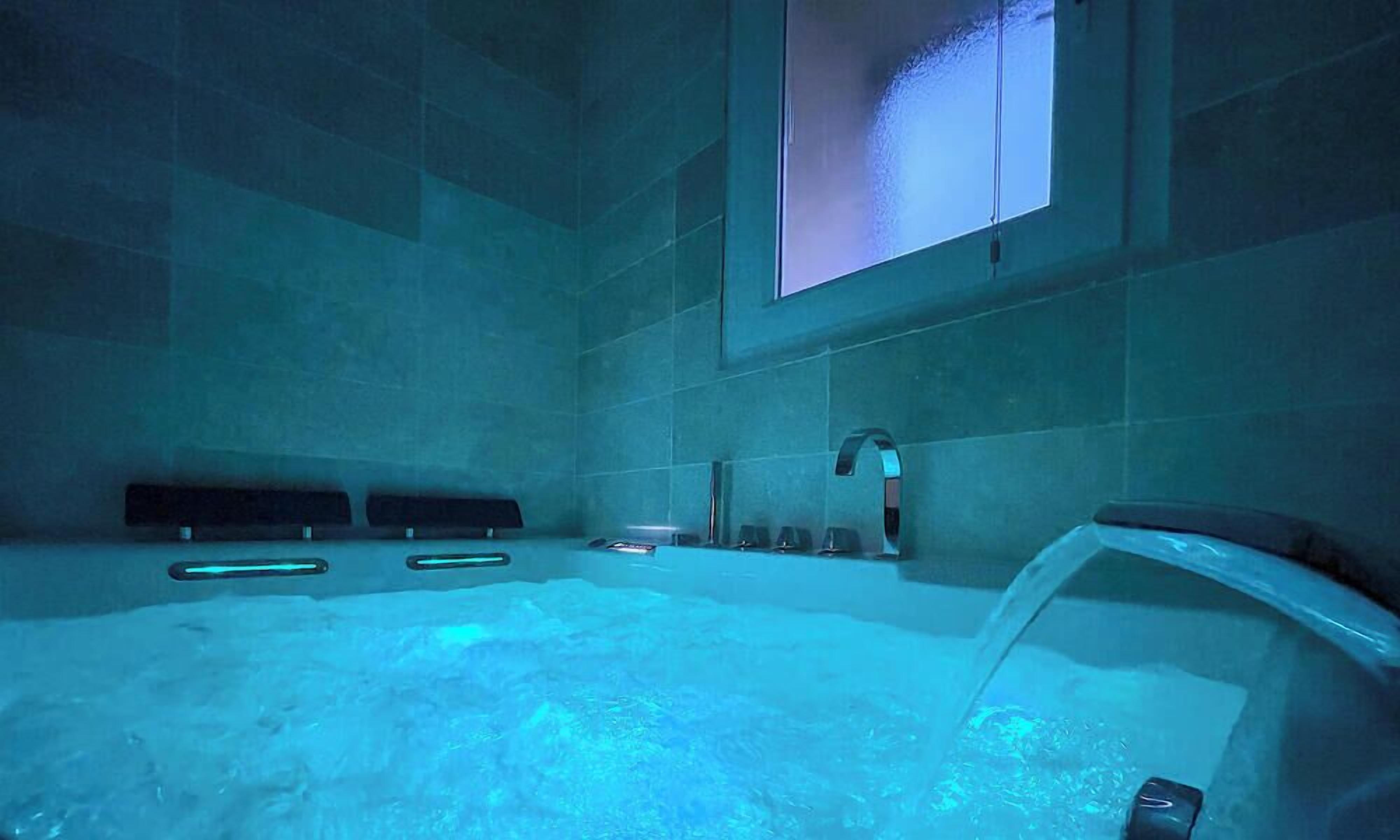 A modern bathroom with a large bathtub, a window, and a wall-mounted sink.