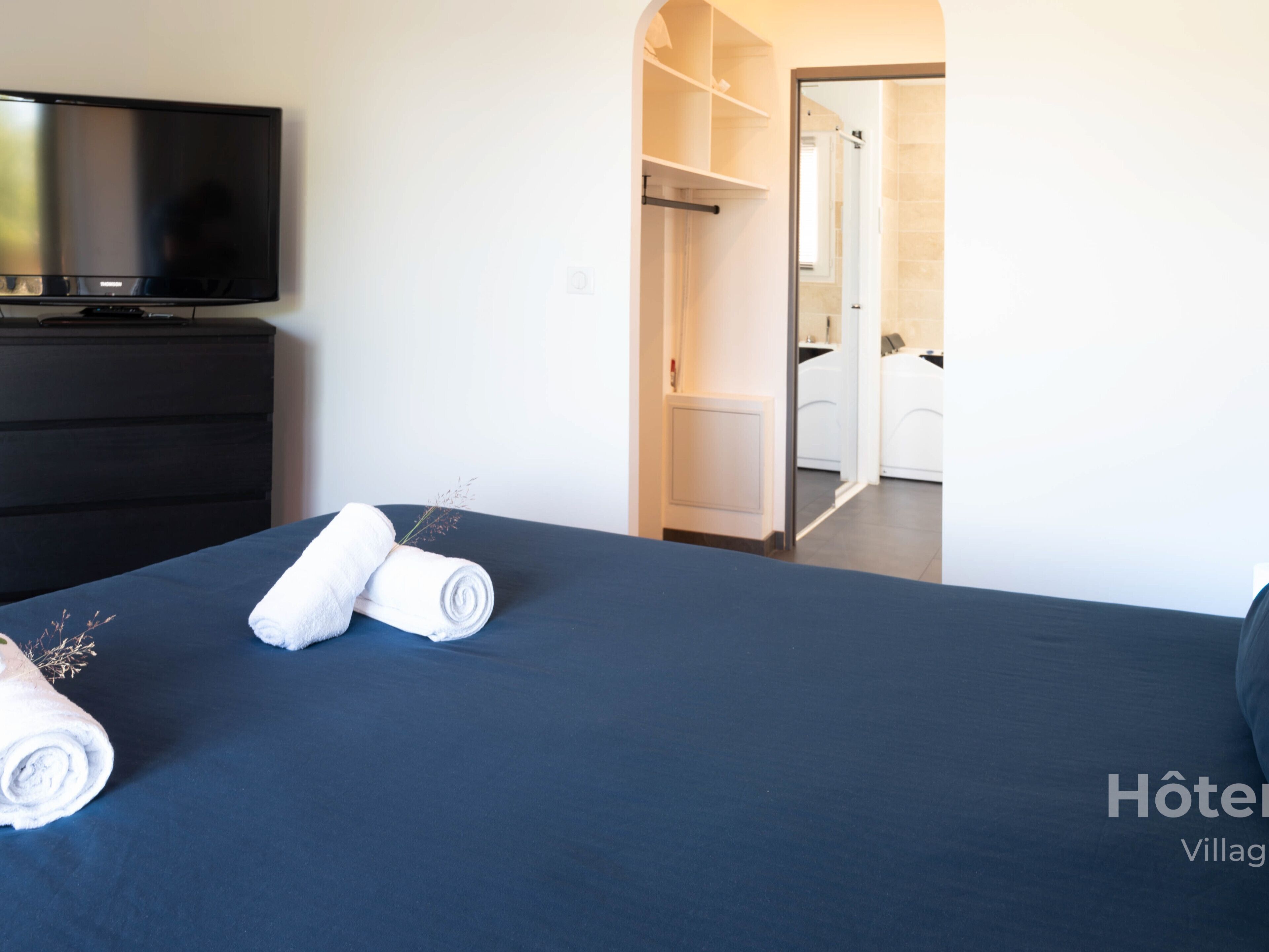 Une chambre d’hôtel avec un lit, un téléviseur posé sur une commode et un dressing.