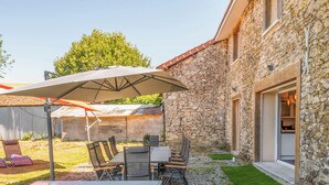 A stone building with a patio area featuring a table, chairs, and umbrellas. - La Vedrenne: Smart Barn near Limoges (Bonnac-la-Côte)
