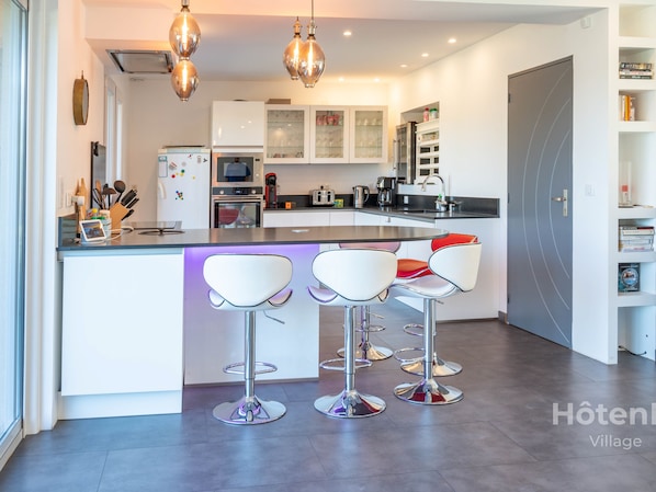 A modern kitchen with white cabinets, a central island with bar stools, and stainless steel appliances.