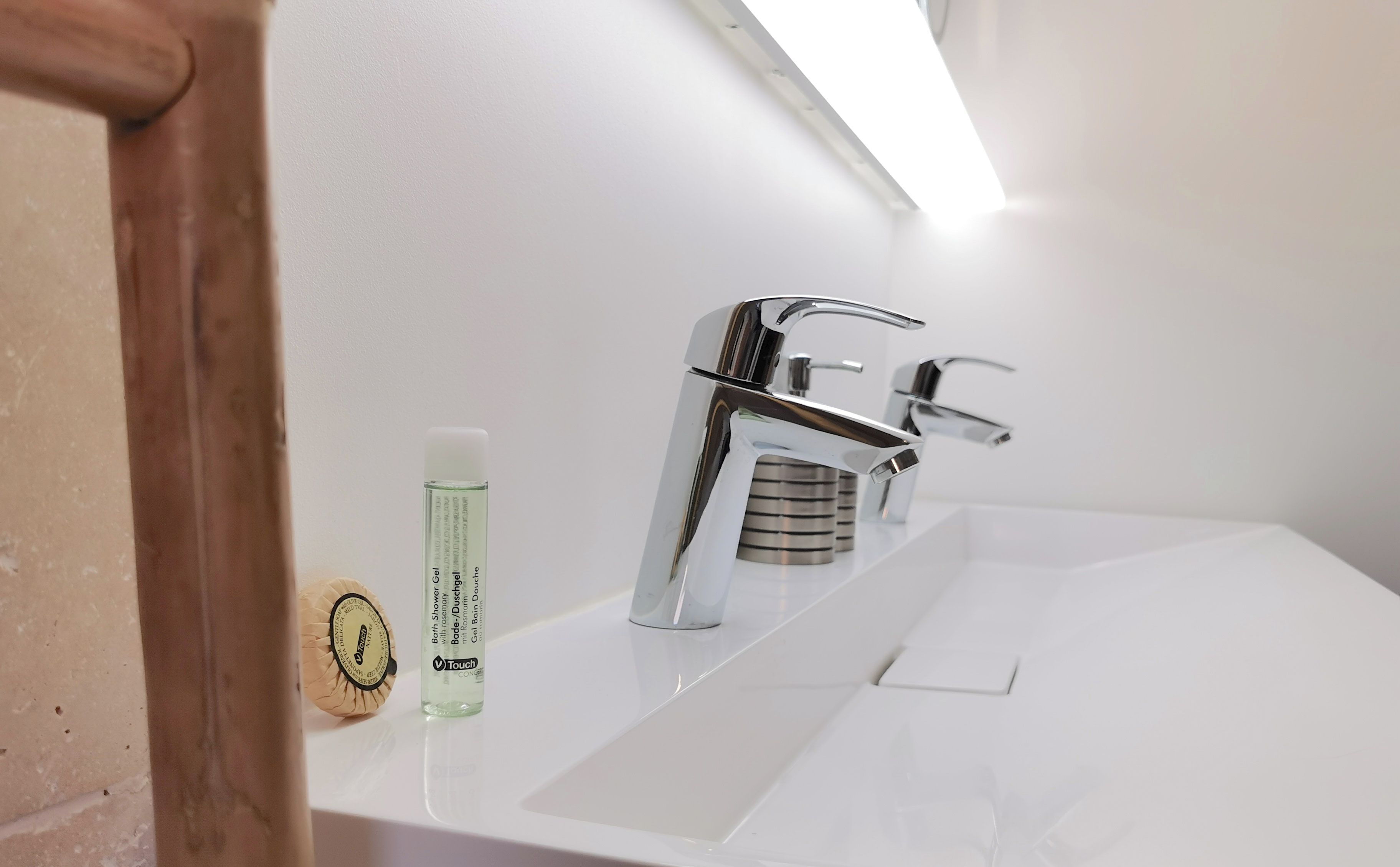 Une salle de bain moderne avec un robinet chromé, un lavabo blanc et une bouteille de gel douche.
