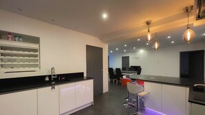 A modern kitchen with white cabinets, a black countertop, and pendant lighting. There is a dining area with a table and chairs. - La Vedrenne: Smart Barn near Limoges (Bonnac-la-Côte)