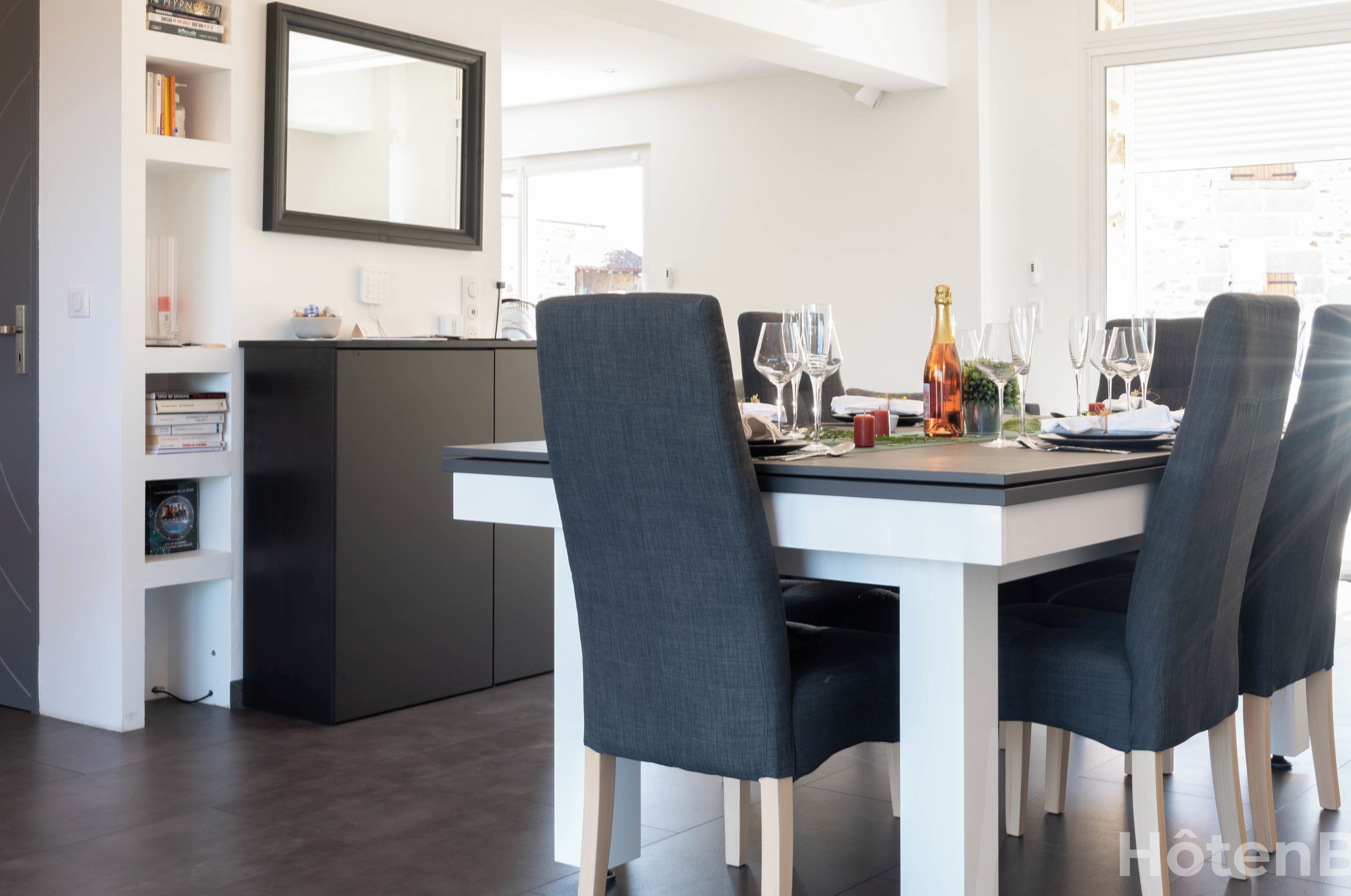 Un'area pranzo moderna con un tavolo bianco apparecchiato per quattro persone, sedie scure e una cucina scura sullo sfondo.