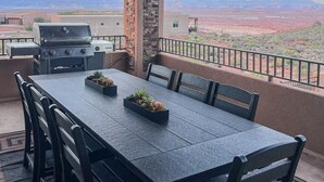 A covered outdoor dining area with a table and chairs, a grill, and a view of a desert landscape. - The Cliff Dweller - 3400sf, 50-Mile Views, Hot Tub (Page)