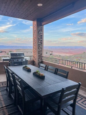 A covered outdoor dining area with a table and chairs, a grill, and a view of a desert landscape.