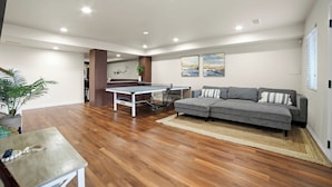 A spacious living area with a ping pong table, grey sofa, and wooden flooring. - The Cliff Dweller - 3400sf, 50-Mile Views, Hot Tub (Page)