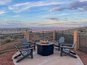 An outdoor seating area with a fire pit and chairs, surrounded by a fence with a view of a desert landscape.