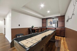 Une table de billard dans une pièce au plancher en bois, un coin repas avec des chaises et un espace cuisine avec des placards.