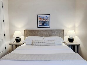 A hotel room with a bed, two bedside tables with lamps, a headboard, and a framed picture on the wall.