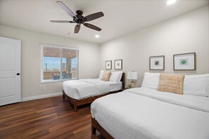 A hotel room with two beds, a ceiling fan, a window with blinds, and framed pictures on the wall.