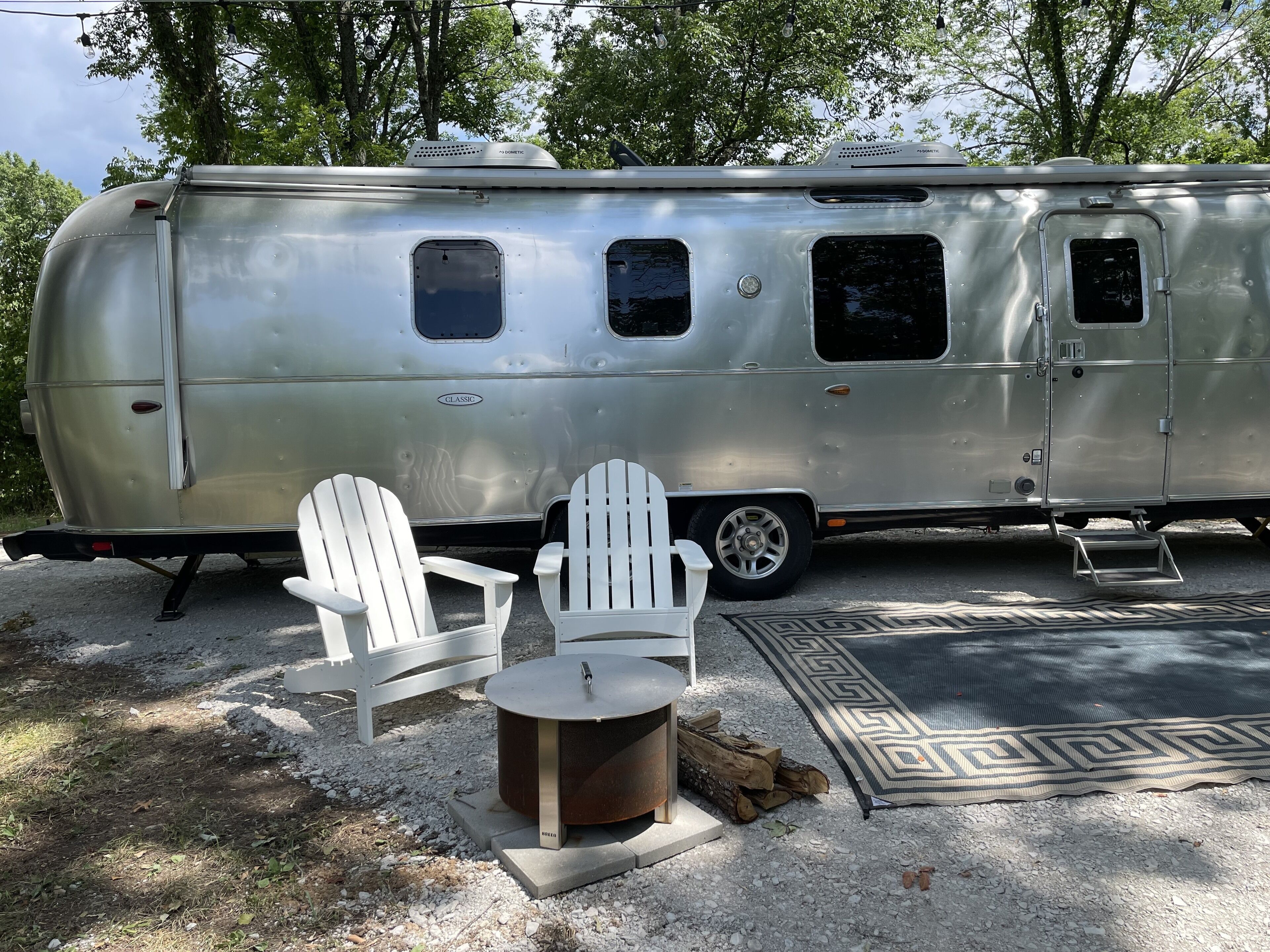 A stationary trailer with a kitchen area, two white chairs, and a small table.