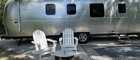 A stationary trailer with a kitchen area, two white chairs, and a small table.