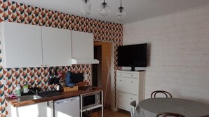 Una cocina funcional con armarios blancos, microondas y lavamanos. Hay una mesa de comedor con sillas y un televisor de pantalla plana montado en la pared.