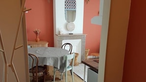 Un comedor con mesa y sillas, una pequeña cocina con mostrador y fregadero, y un espejo colgado en la pared sobre el mostrador.
