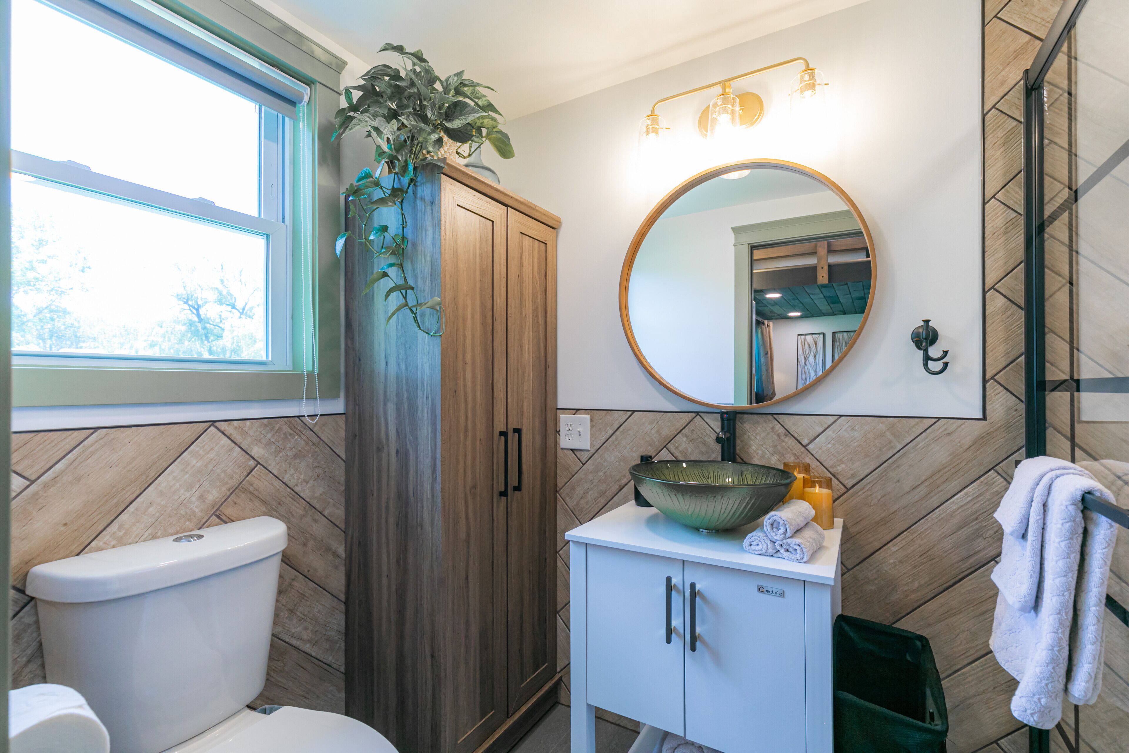 Un baño con inodoro, un mueble de madera, lavabo, espejo y toallero.
