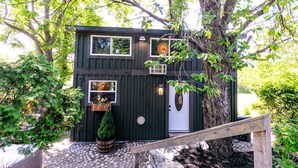 Een houten vakantiehuis met twee verdiepingen, een veranda, een klein raam en een deur.