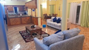 A living room with a sofa, a coffee table, and a dining area with chairs and a table. - Awesome Homes - Panoramic Heights (Gros Islet)