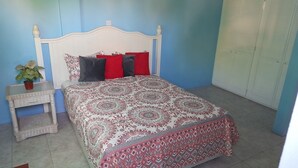 A bedroom with a bed, a nightstand, a potted plant, and a wardrobe. - Awesome Homes - Panoramic Heights (Gros Islet)