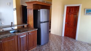 A kitchen with wooden cabinets, a stainless steel refrigerator, a sink, and a patterned floor. - Awesome Homes - Panoramic Heights (Gros Islet)