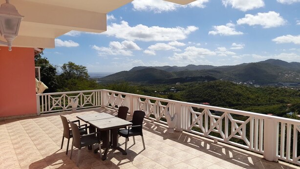 A terrace with a table and chairs, overlooking a mountainous landscape. - Awesome Homes - Panoramic Heights (Gros Islet)