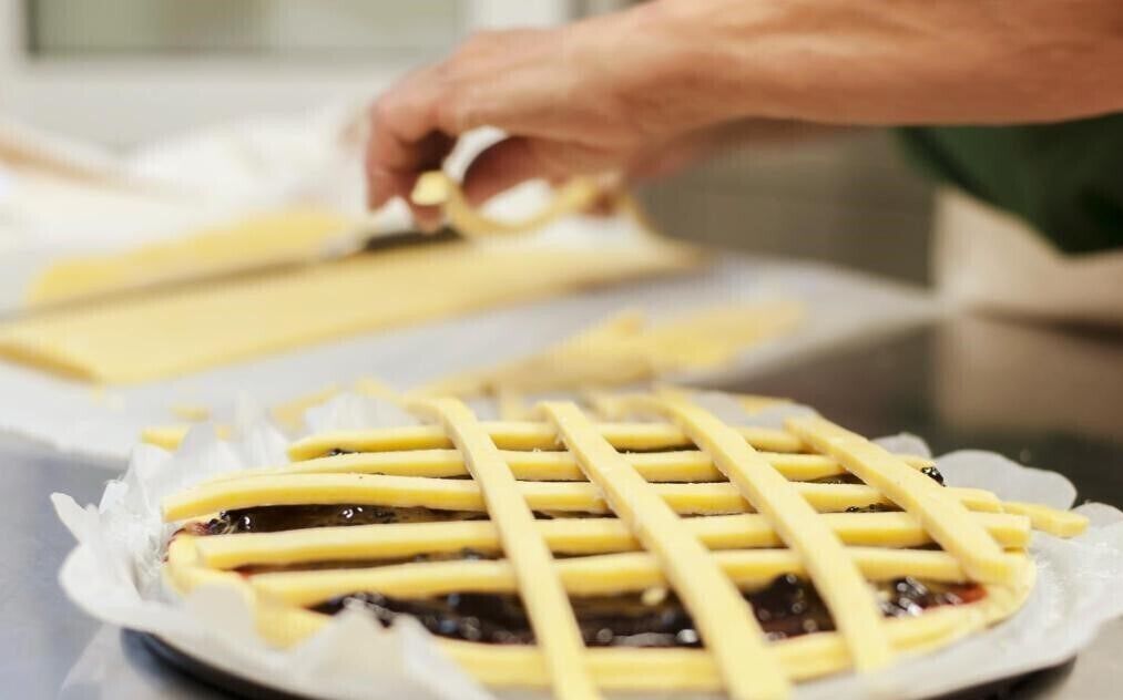 A person placing a lattice on a pie crust.