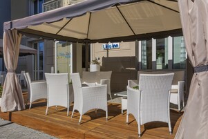 An outdoor seating area with white wicker furniture under a large umbrella, a sign for 'Lido Inn', and a building facade in the background.