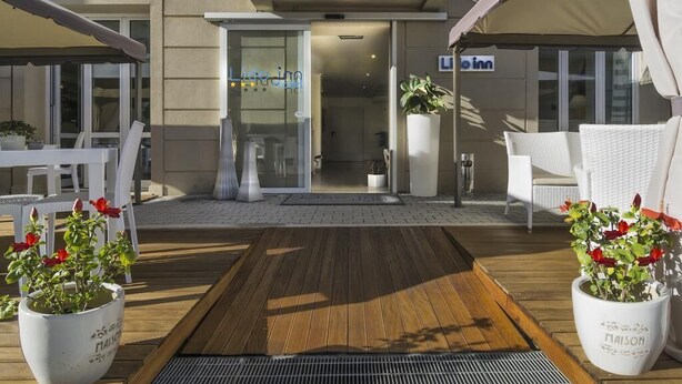 A hotel entrance with a wooden deck, white chairs, and potted plants. - Hotel Lido Inn (Camaiore)
