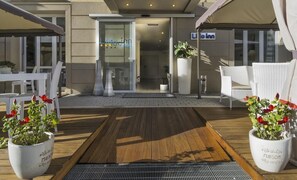 A hotel entrance with a wooden deck, white chairs, and potted plants. - Hotel Lido Inn (Camaiore)