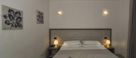 Un dormitorio moderno con una cama grande, dos lámparas de noche y dos luces fijadas a la pared.