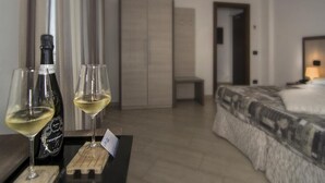 A modern hotel room with a bed, a wooden nightstand, and a table with wine glasses and a bottle. - Hotel Lido Inn (Camaiore)
