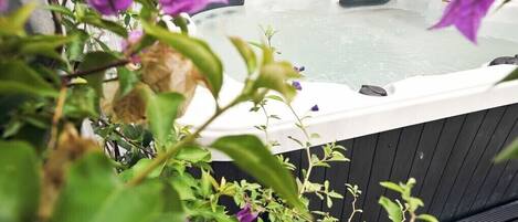 A hot tub surrounded by lush greenery and purple flowers.