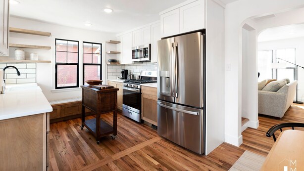 A modern kitchen with white cabinets, stainless steel appliances, and a wooden floor.