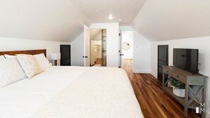 A bedroom with a large bed, wooden flooring, a TV, and a walk-in closet.