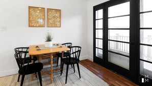 A dining area with a wooden table and black chairs, two framed artworks on the wall, and a large window with multiple panes.