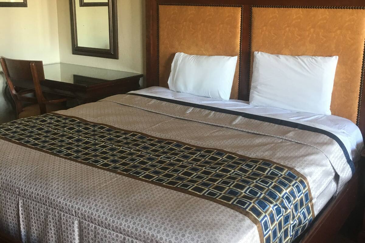 Hotelkamer met een groot bed, een houten hoofdbord, een bureau met stoel, en twee afbeeldingen in lijsten aan de muur.