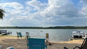 A lakeside view with beach chairs, a dock, and a boat.