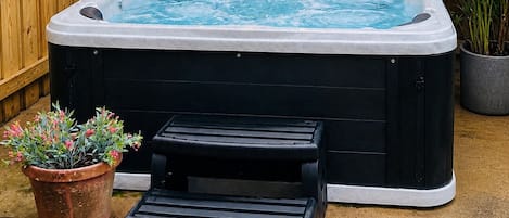 A hot tub with a black cover, a wooden fence, and a small table with a potted plant.