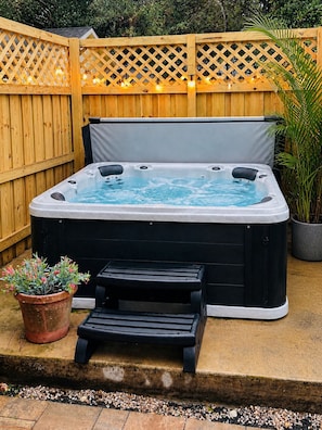Un jacuzzi con tapa negra, cerca de una valla de madera y una pequeña mesa con una planta en maceta.