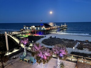 A pier extending into the ocean with a building at the end, a beach area with pathways, and palm trees. - Boardwalk LUX Shoreline/ Prime Location (Myrtle Beach)