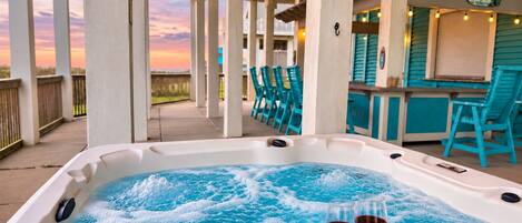 Un jacuzzi con dos copas de vino tinto, rodeado de sillas color turquesa y una terraza de madera.