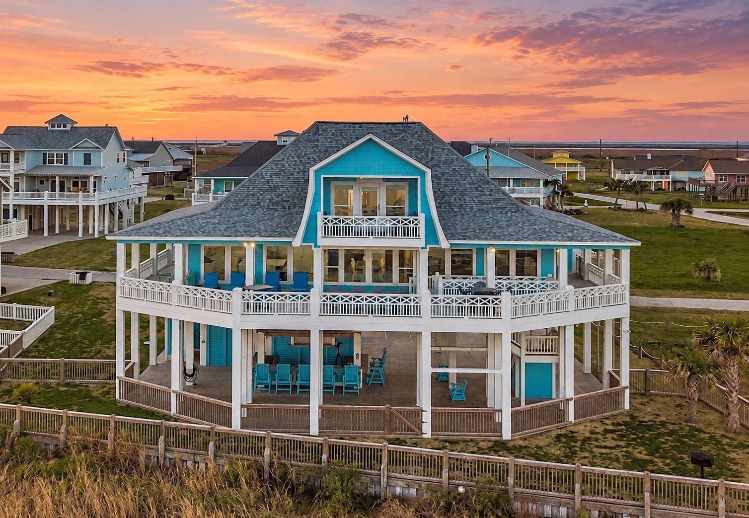 A two-story beachfront house with a balcony, multiple windows, and a covered porch area.