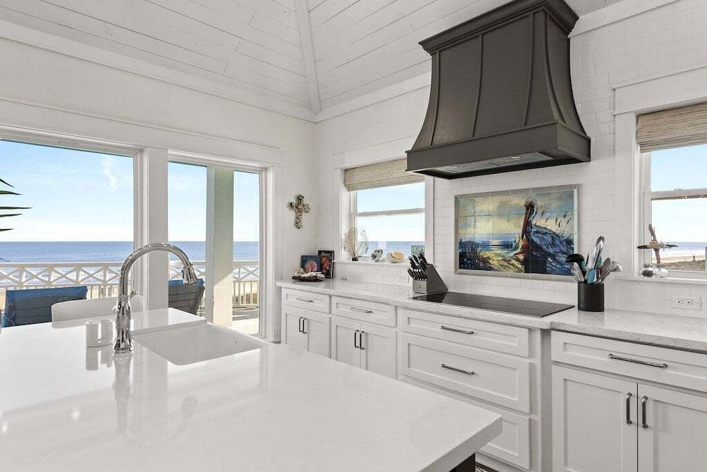 A spacious kitchen with white cabinetry, a large island with a sink, and a view of the ocean through large windows.
